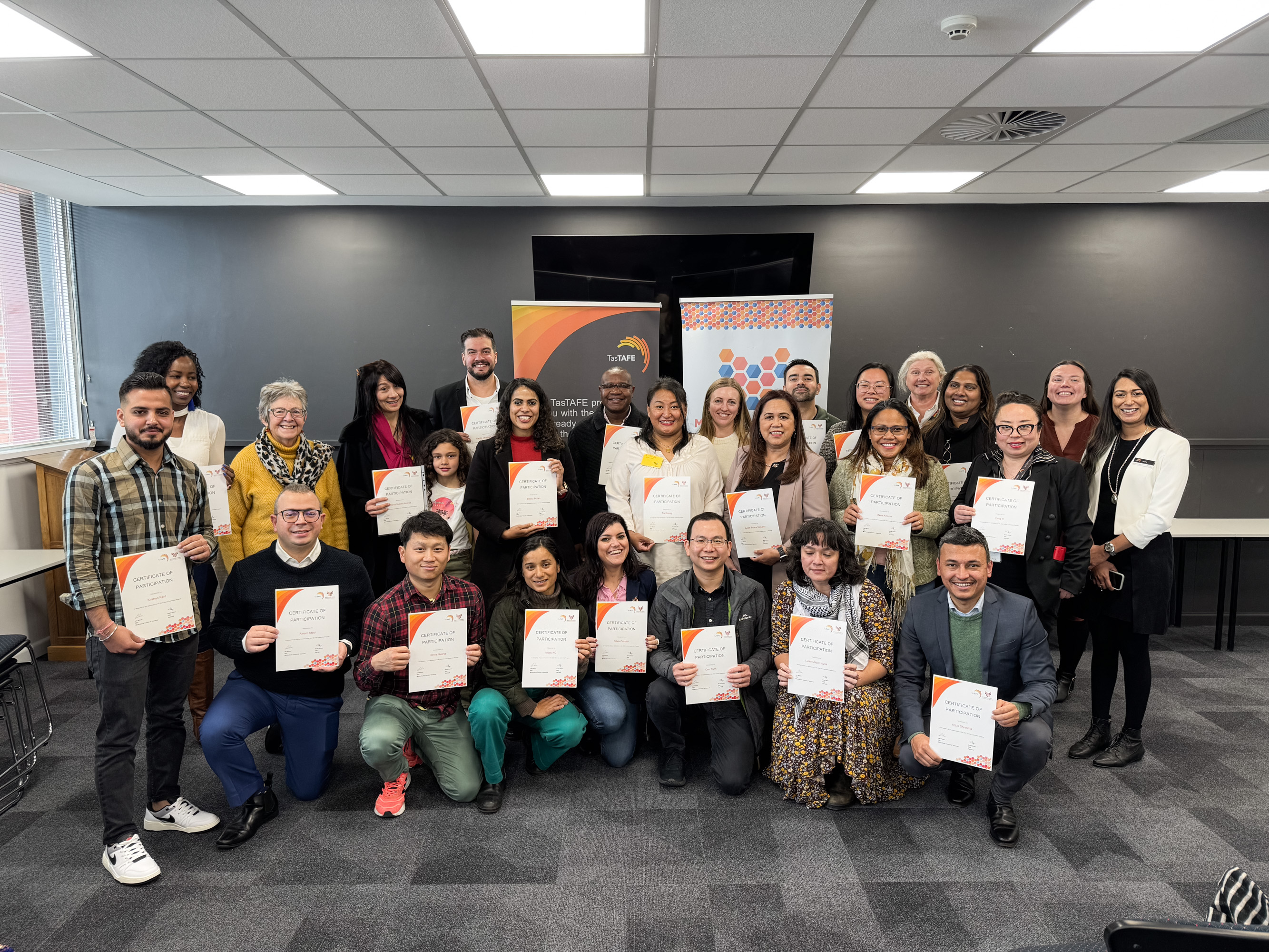 Diverse group of people posing for a photo inside, each holding a certificate