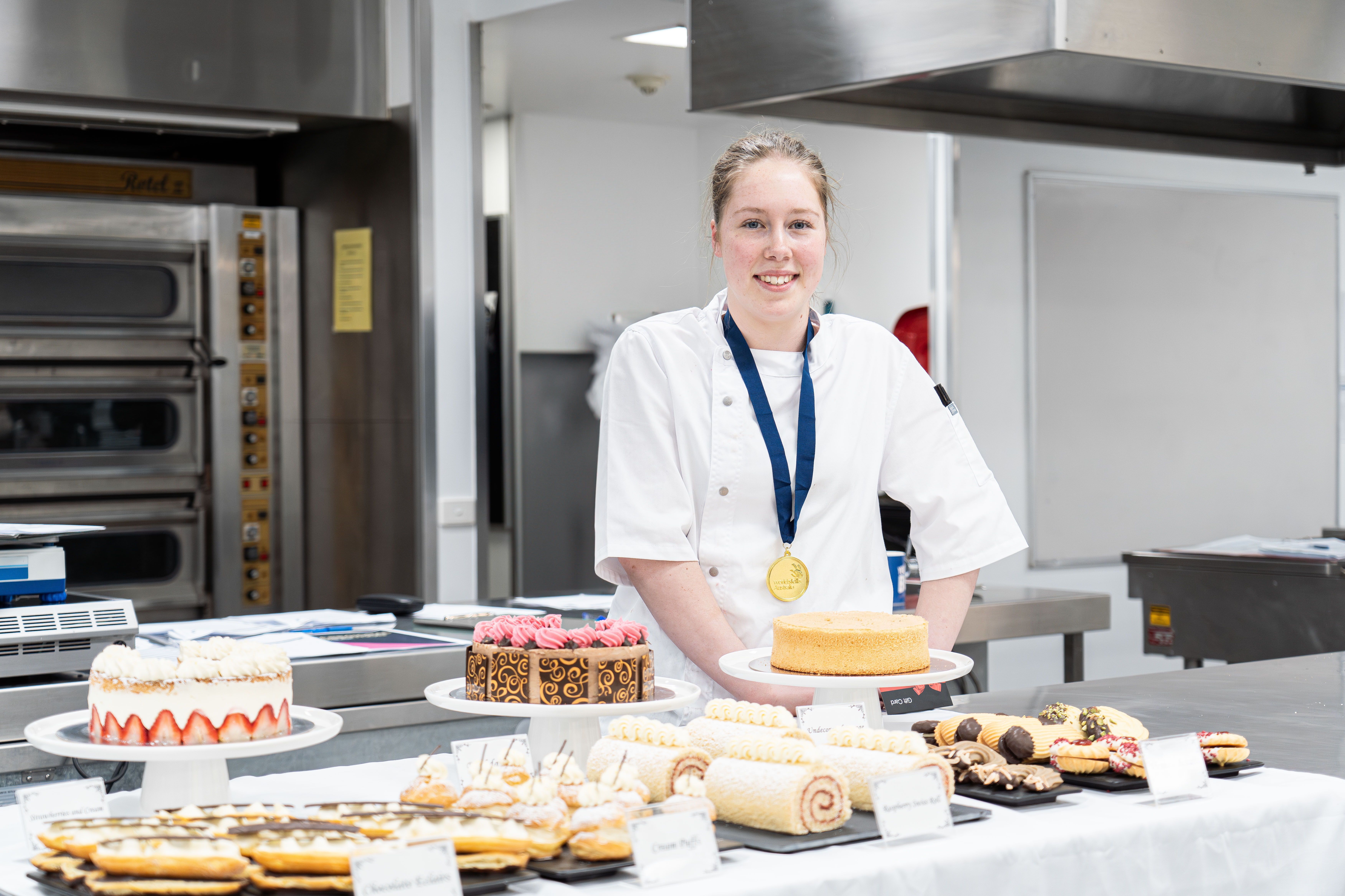 Eve Charlesworth wearing her medal and standing in front of a range of desserts 