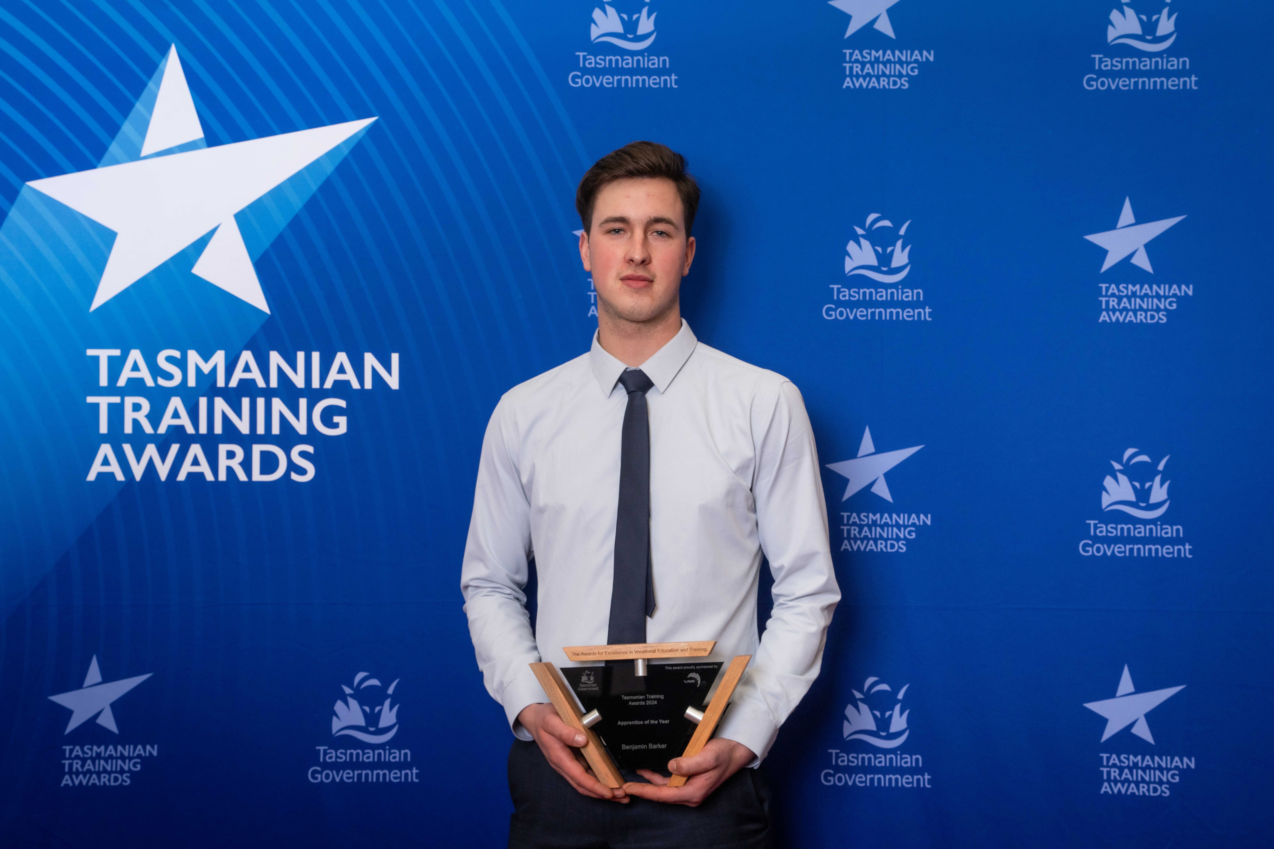 Benjamin Barker holding a trophy with  Tasmanian training awards blue background behind him