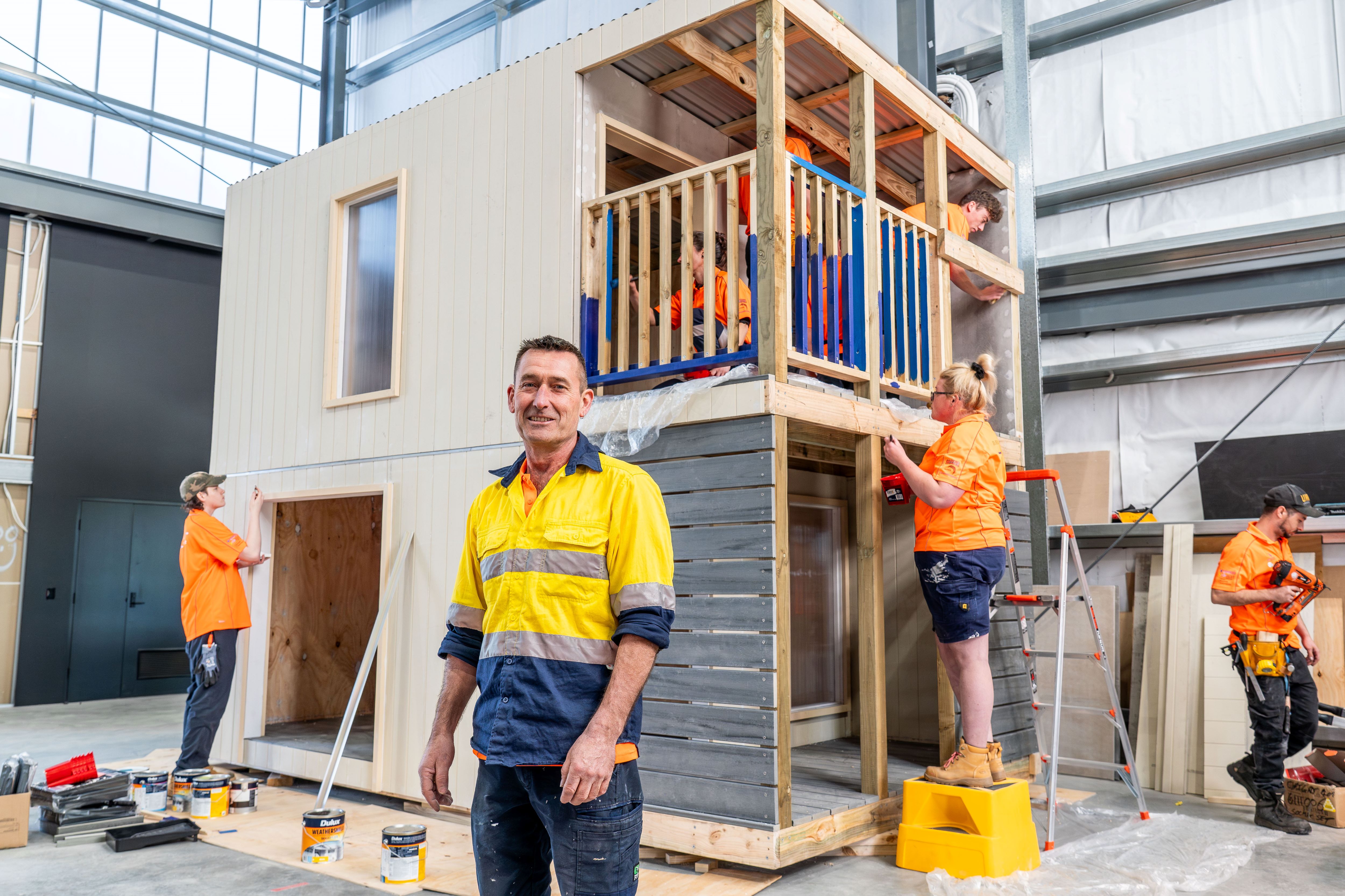 People building a 2 storey cubby house in  a warehouse. 