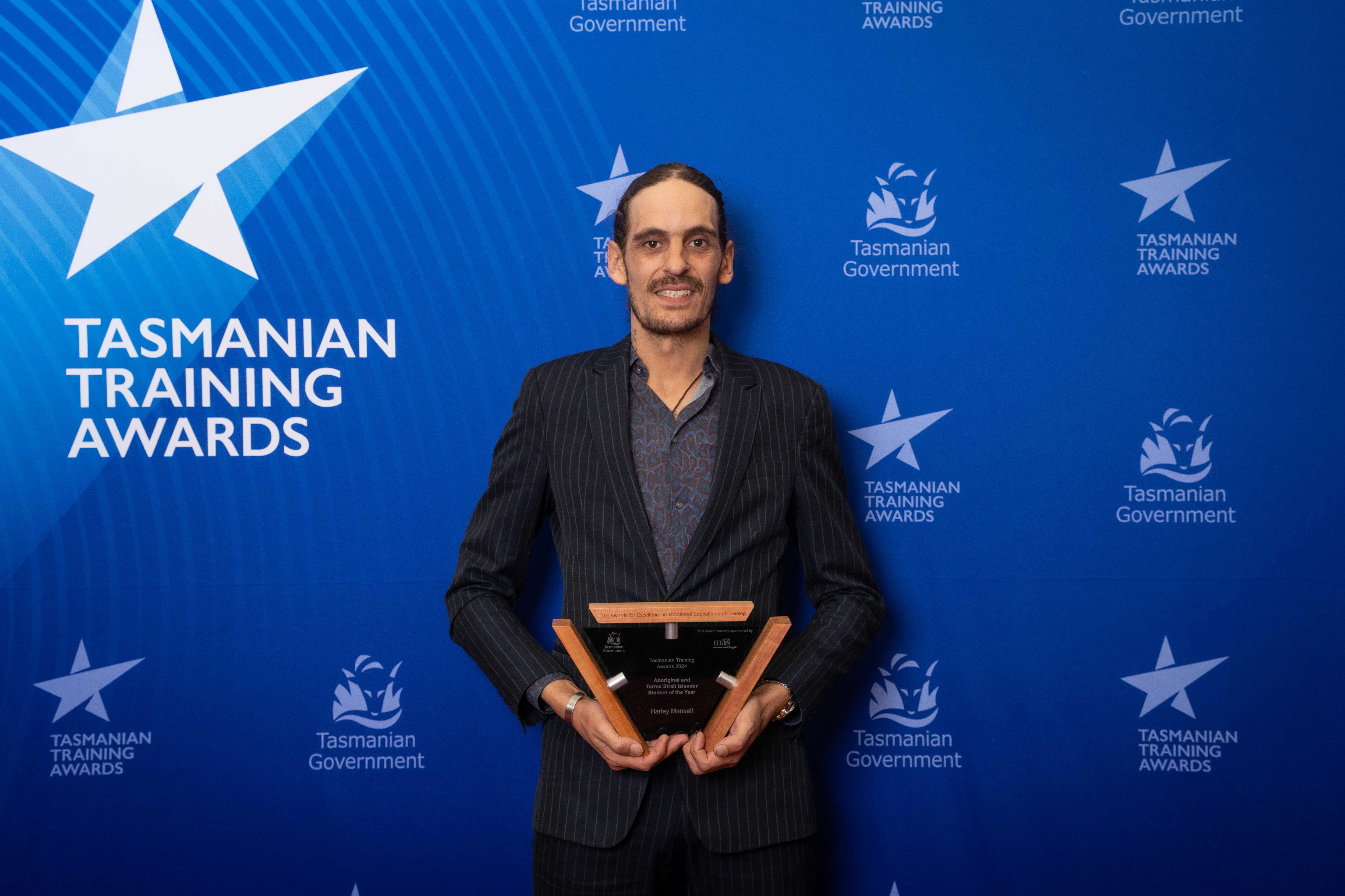 Harley Mansell holding a trophy with  Tasmanian training awards blue background behind him