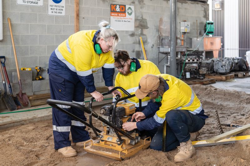 3 people in hi vis clothing working on a compactor in sand 