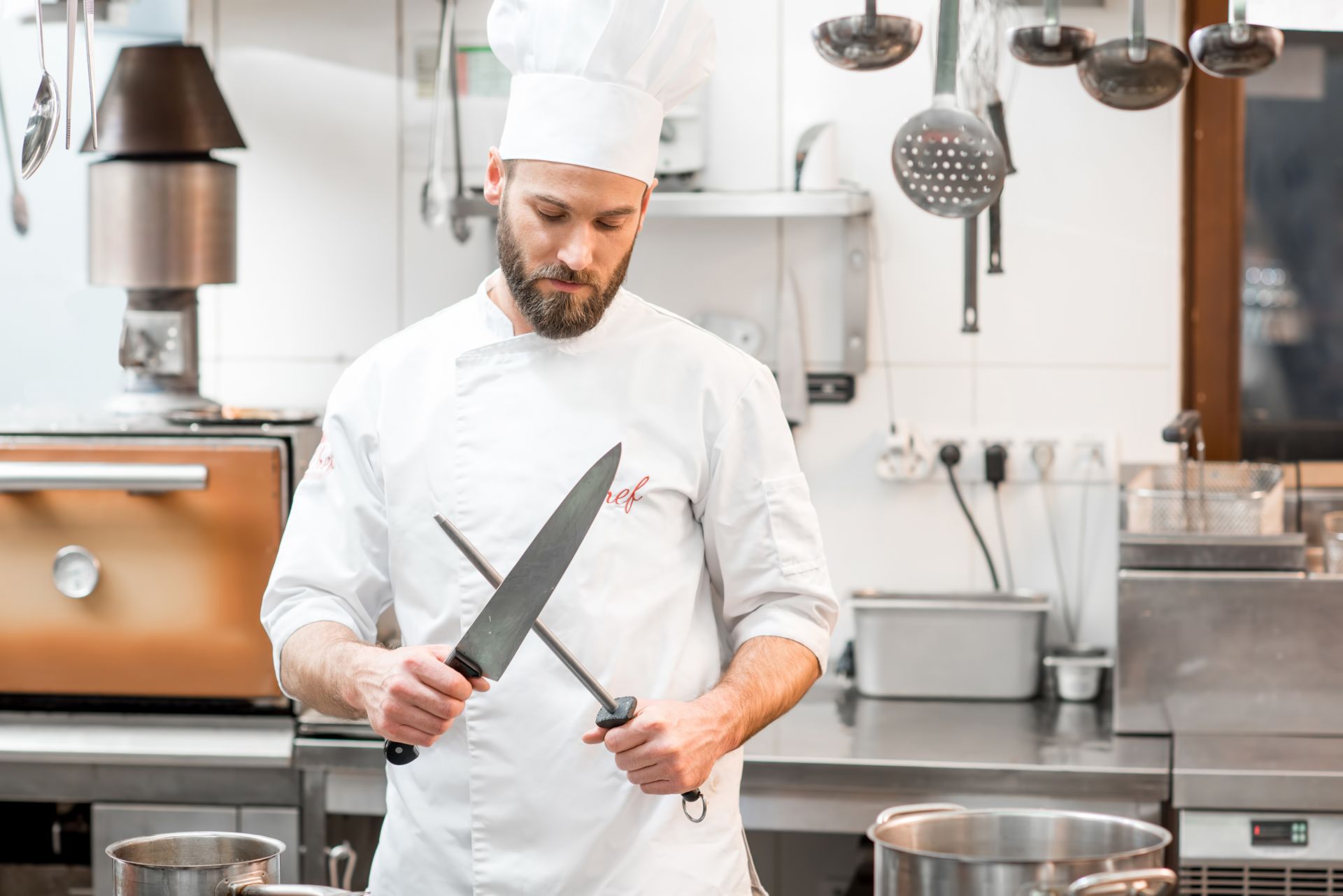 Man wearing chef whites sharpening a knife in the kitchen