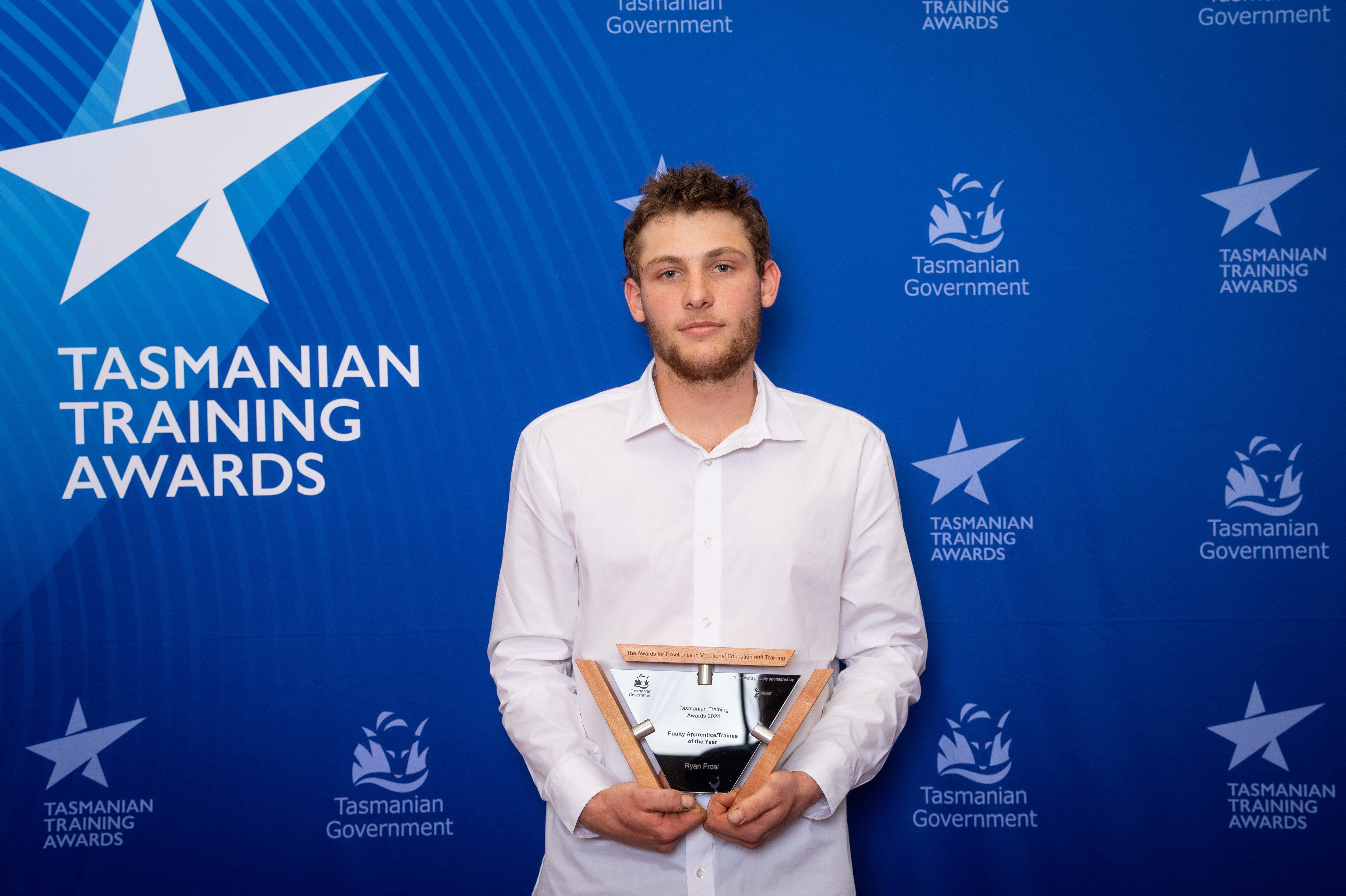 Ryan Frosi holding a trophy with  Tasmanian training awards blue background behind him