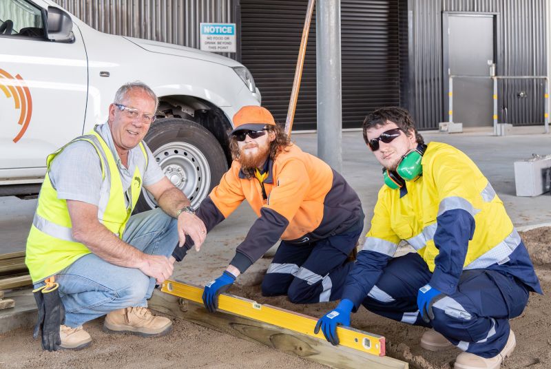 Teacher and 2 students checking if the sandy ground is level with a ute in the background