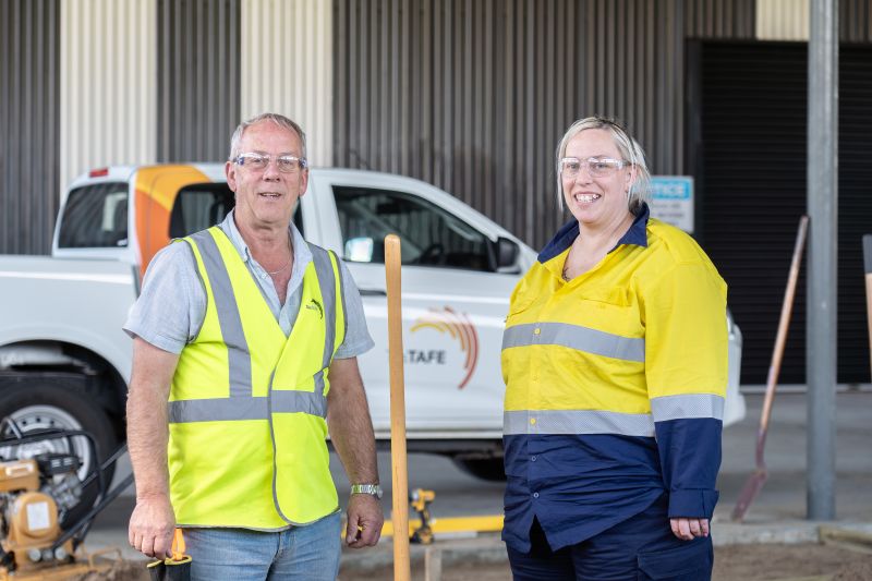 Man and woman pose for photo wearing hi vis clothing and a TasTAFE ute in the background