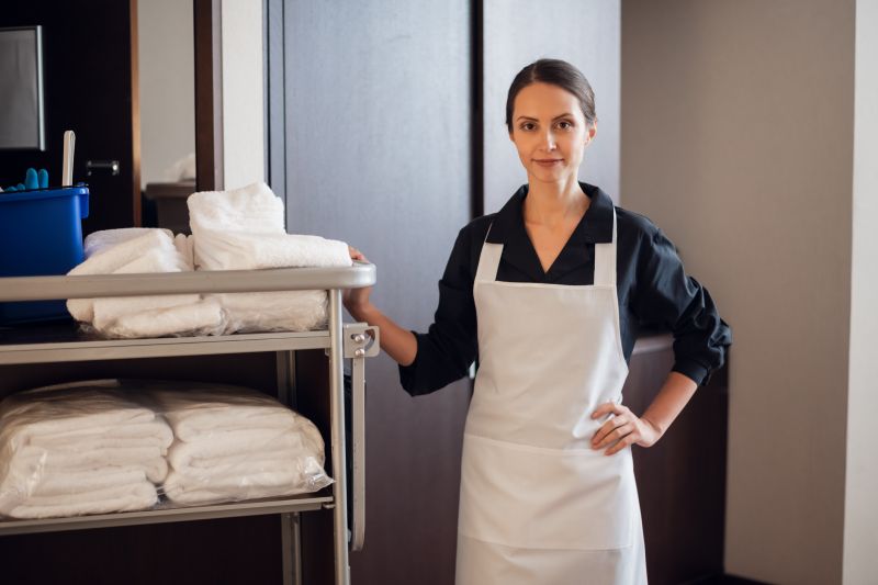 Housekeeper smiling standing beside a housekeeping trolley with towels and cleaning supplies