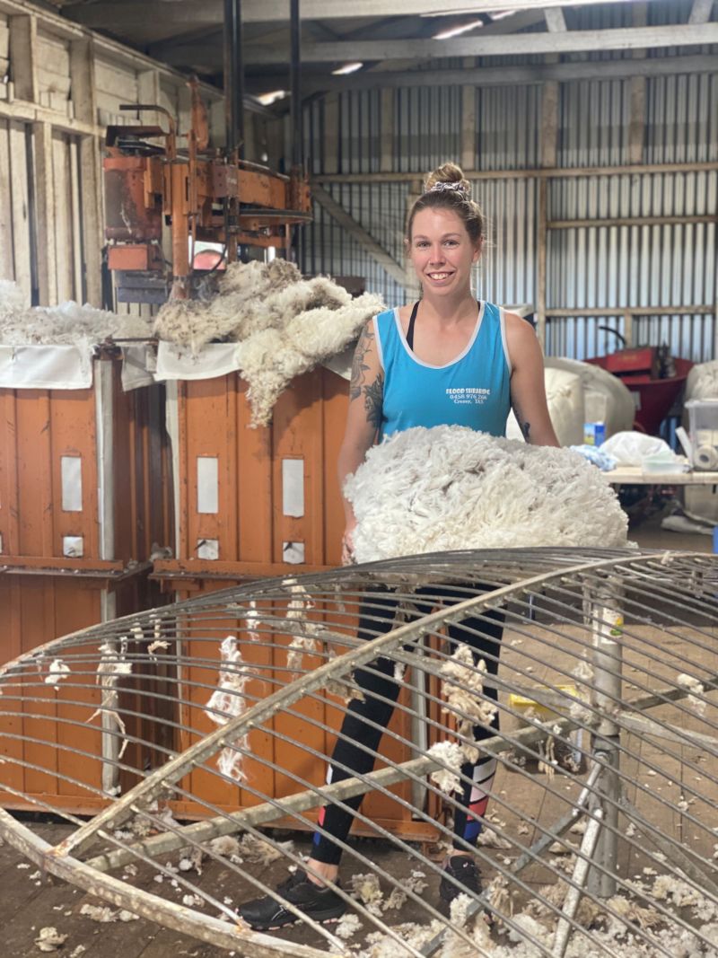 Woman standing with clump of wool in a shed.