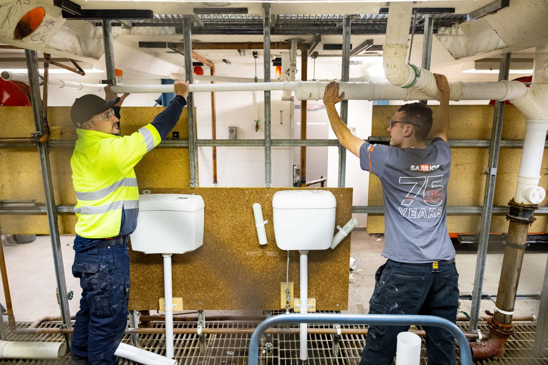 2 people working on a white PVC pip above their heads