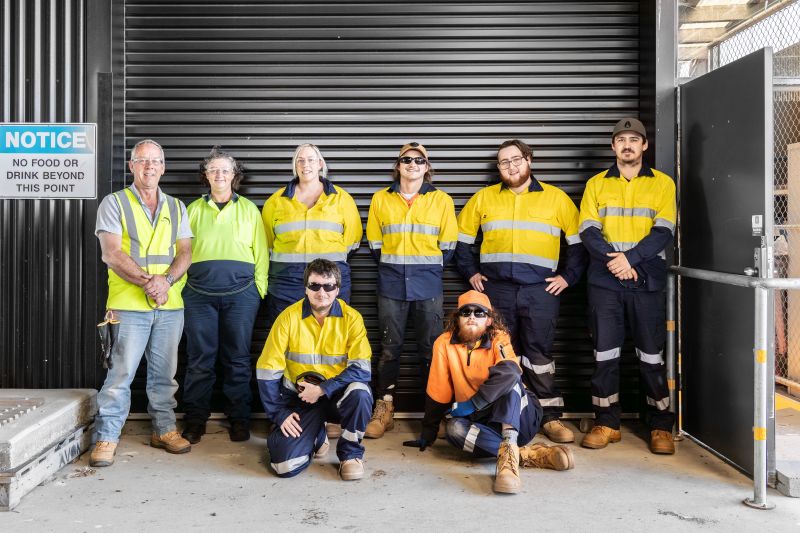 group of people wearing Hi vis clothing pose for a photo in front of a workshop roller door